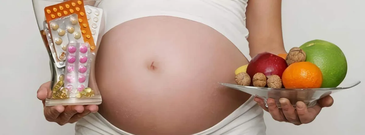 Mujer embarazada sostiene un vaso lleno de suplementos y un plato con fruta